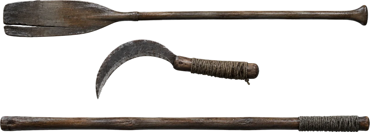 Dayung kayu yang retak, sabit tangan bergagang tali, dan tongkat kayu keras tergantung berjajar.